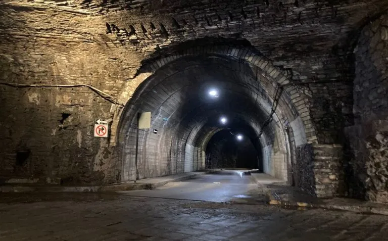 una toma amplia del interior de uno de los túneles, con sus muros de piedra y la iluminación que conduce hacia la salida.
